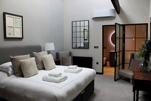 A hotel room with a large bed, a desk, a chair, a lamp, and a mirror. - The Merchant's Yard (Tideswell)