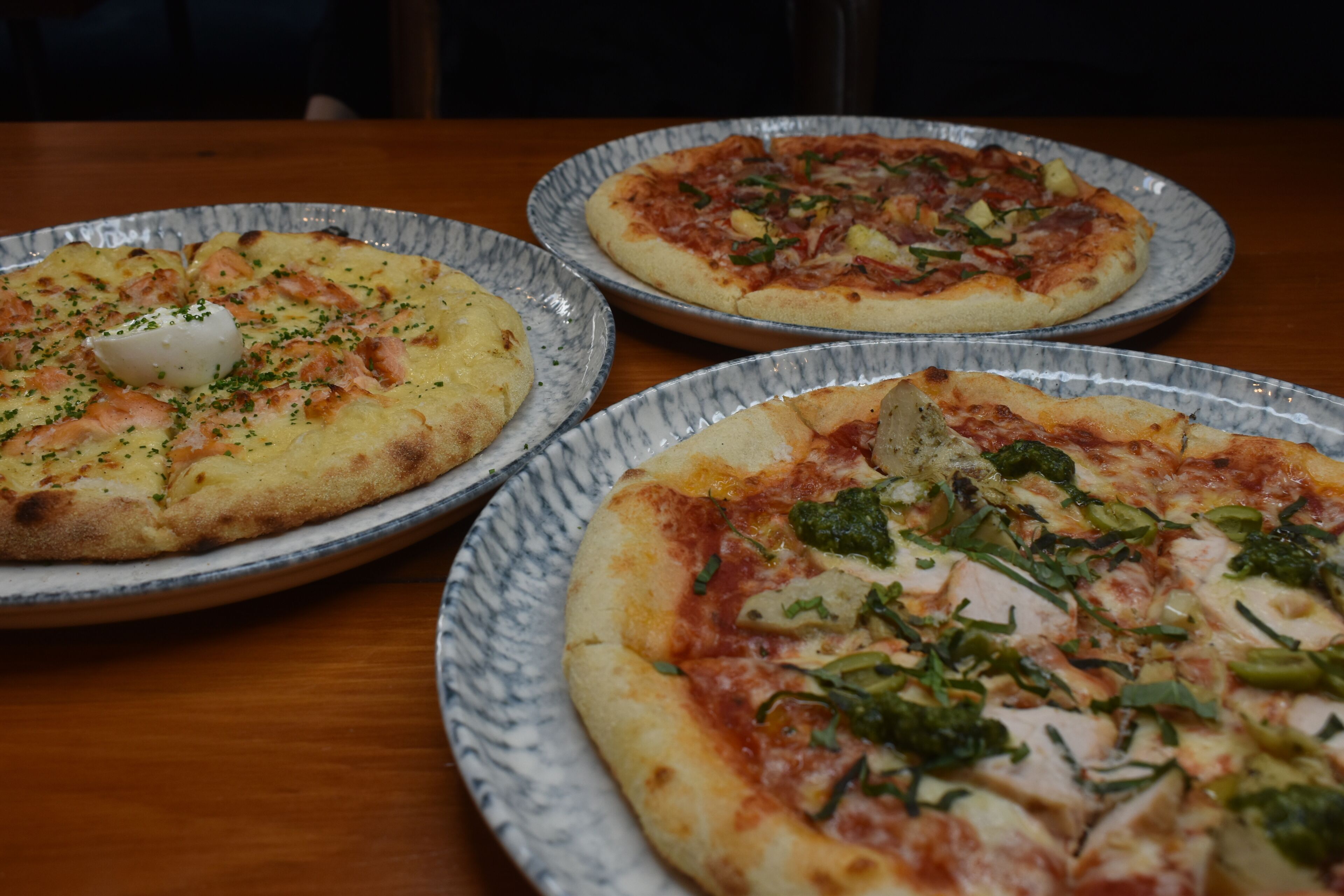 Three pizzas on plates with different toppings.