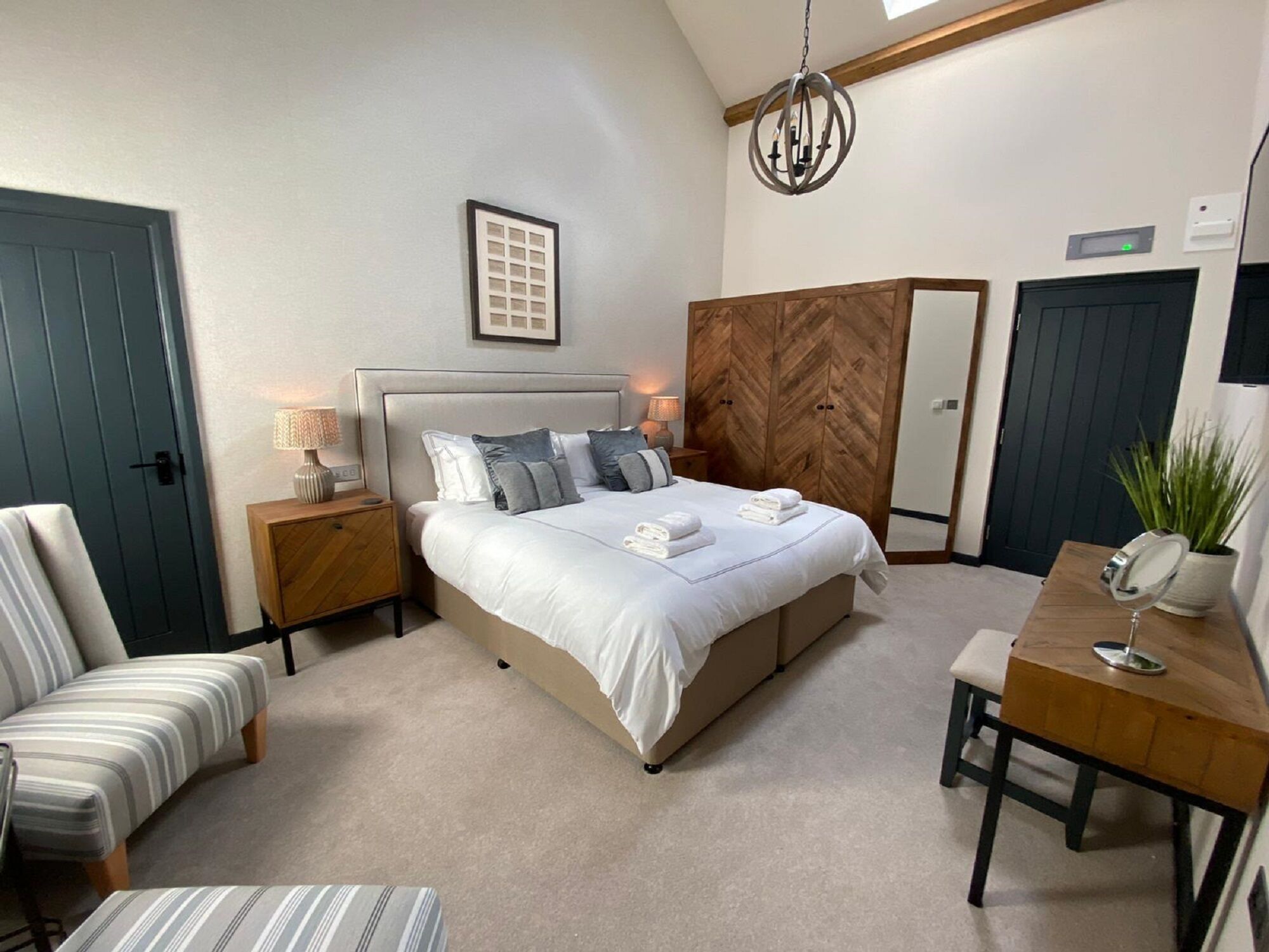 Een slaapkamer met een bed, nachtkastjes, een stoel, een bureau, een spiegel, een kamerplant en een houten garderobe.