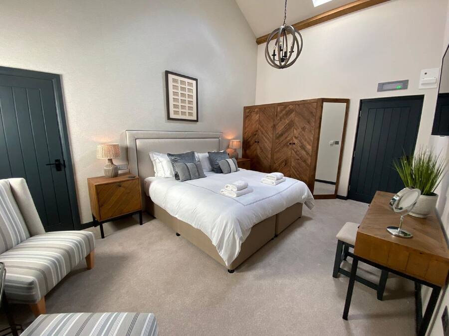 Een slaapkamer met een bed, nachtkastjes, een stoel, een bureau, een spiegel, een kamerplant en een houten garderobe.