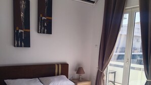 A neatly made bed with white linens and towels, a bedside lamp, and artwork on the wall. - Beachfront  • 4 Guests • Fast WiFi • AC • Near Airport – Artemis Blue Escape (Artemis)