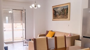 A dining area with a wooden table and chairs, a painting on the wall, and a modern kitchen in the background. - Beachfront  • 4 Guests • Fast WiFi • AC • Near Airport – Artemis Blue Escape (Artemis)