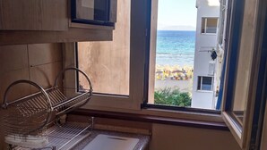 A kitchen with a window view of a beach and buildings. - Beachfront  • 4 Guests • Fast WiFi • AC • Near Airport – Artemis Blue Escape (Artemis)