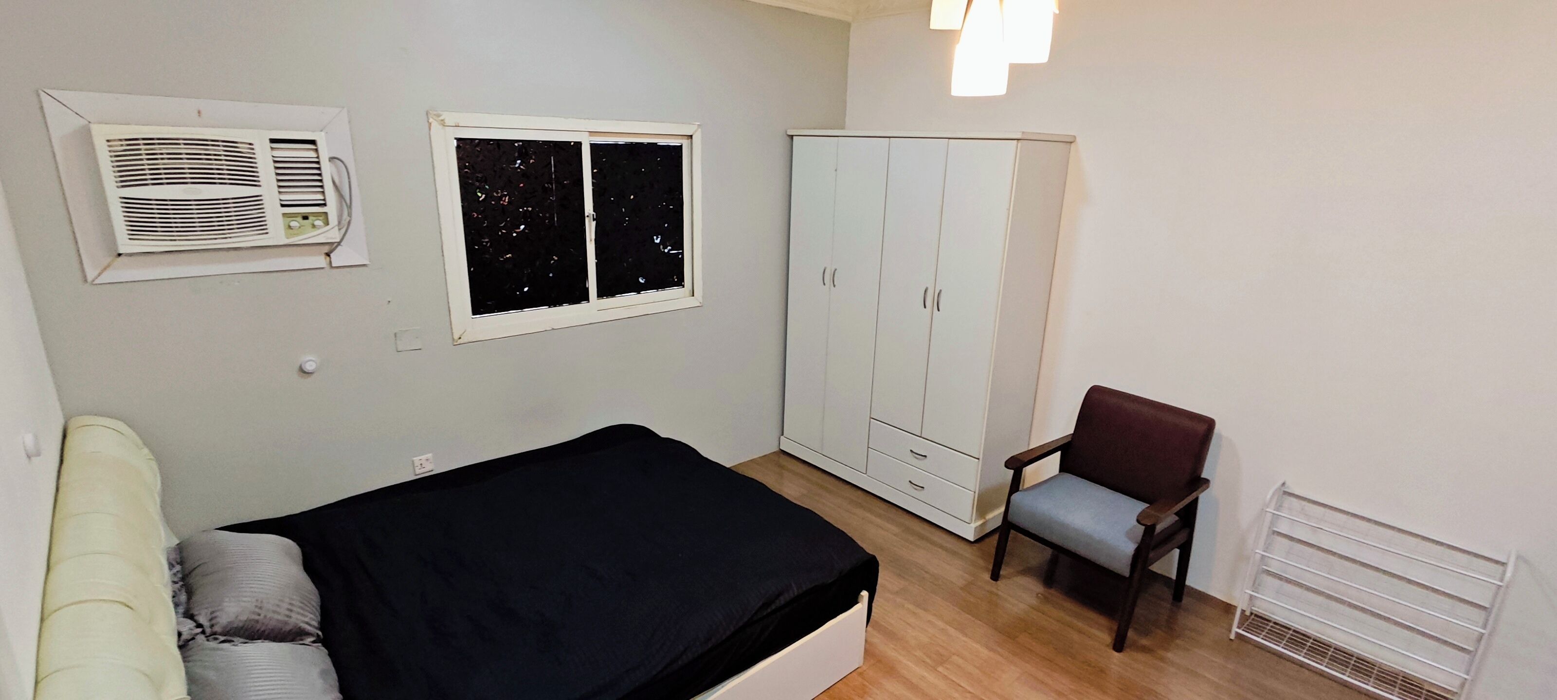 A bedroom with a bed, a chair, a wardrobe, and an air conditioning unit.