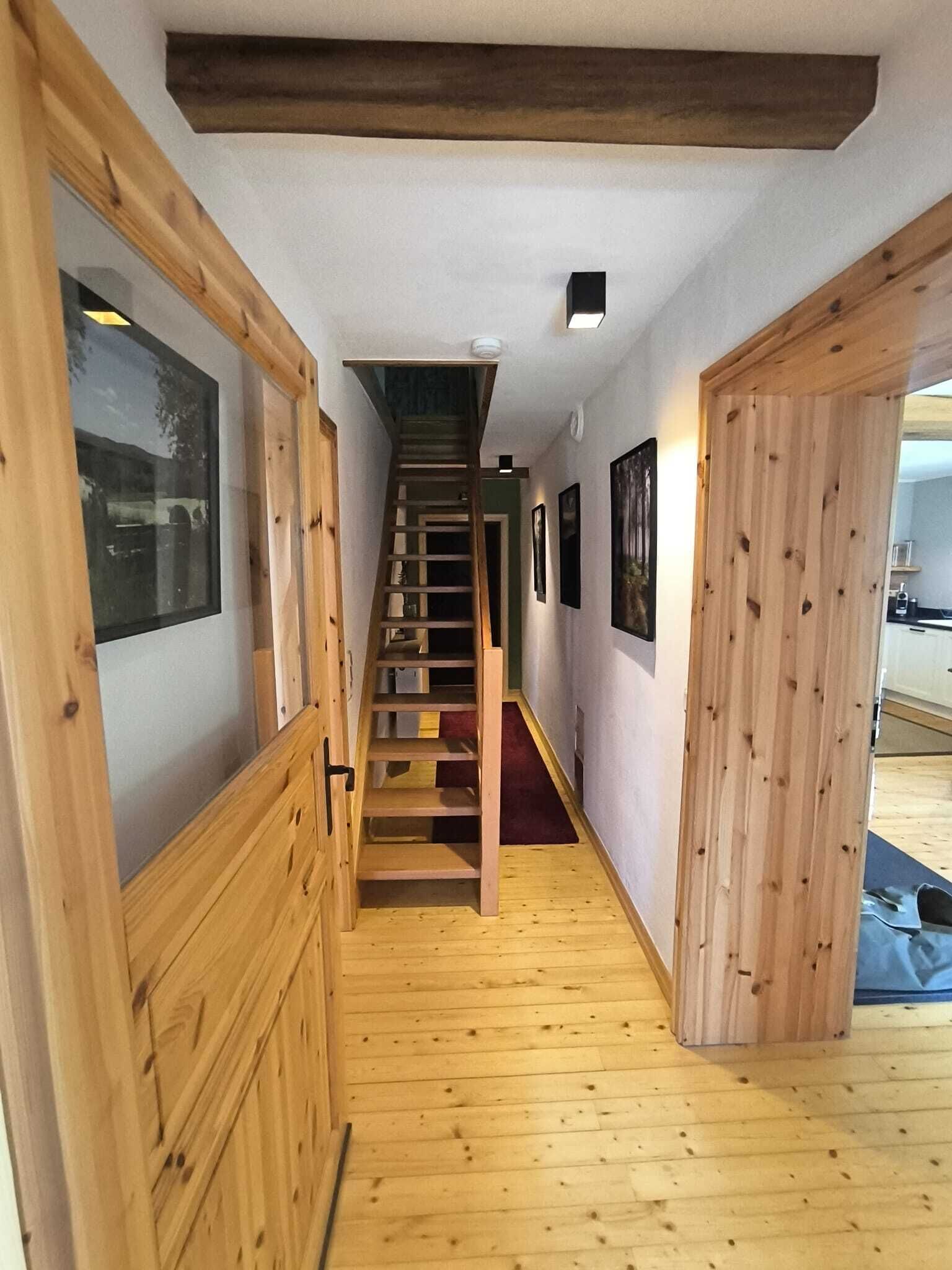 A wooden staircase leading to a second floor, flanked by wooden paneling and framed pictures on the walls.