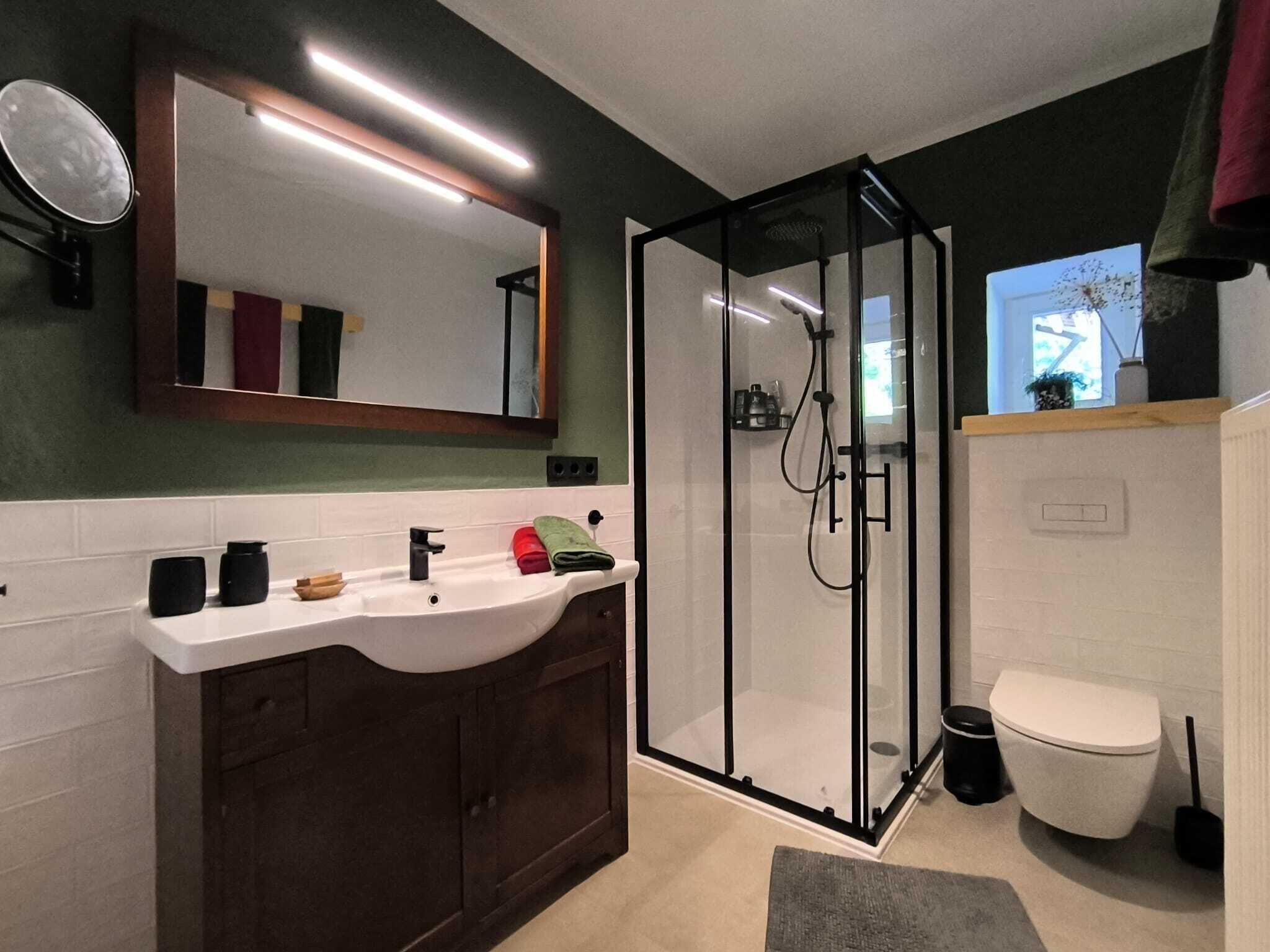 Une salle de bain avec une douche à parois de verre, un lavabo blanc, des meubles en bois foncé et un miroir au-dessus du lavabo.