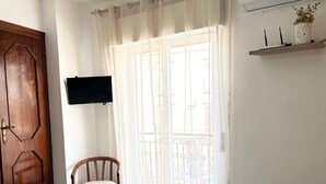 Un dormitorio con cama, una silla, un televisor y un equipo de aire acondicionado.
