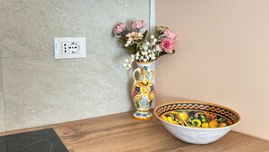Una encimera de cocina con una placa de inducción negra, un florero blanco con flores rosadas y un tazón colorido.