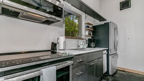 Une cuisine moderne dotée d’appareils électroménagers en acier inoxydable, d’un four encastré et d’une fenêtre offrant une vue sur les arbres.