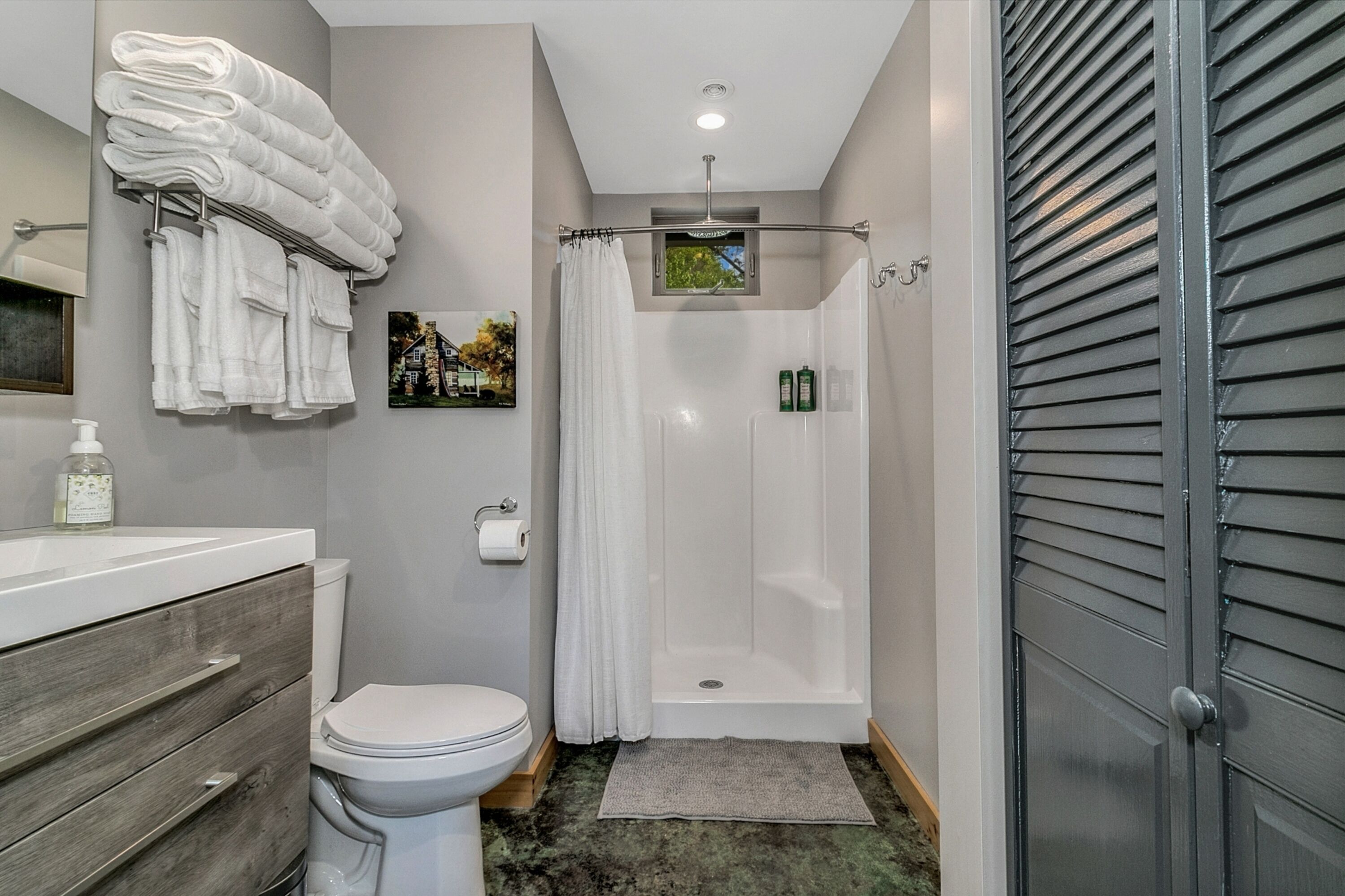 A bathroom with a toilet, a sink with a wooden cabinet, a shower with a glass door, and a towel rack with folded towels.