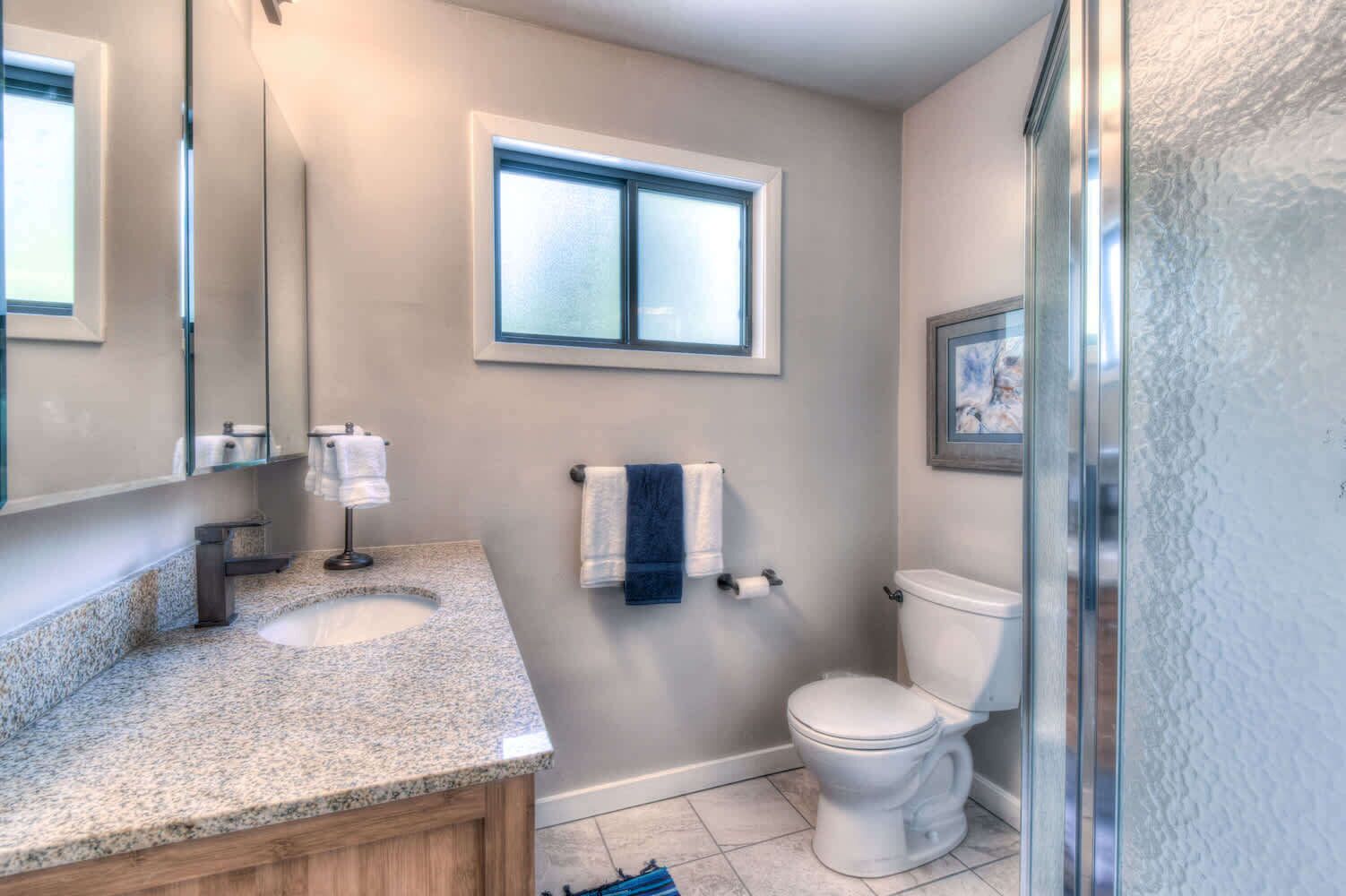 Une salle de bain avec un comptoir en granit, un lavabo double, des toilettes et une fenêtre.