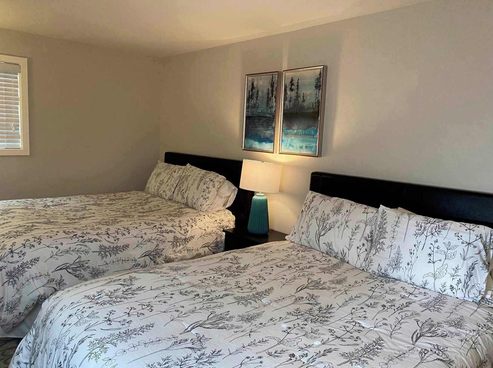 A double bed with floral bedding, a bedside lamp, and two framed pictures on the wall.