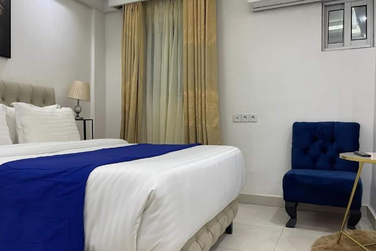 A bedroom with a large bed, a blue chair, a small table, and a leopard artwork on the wall.