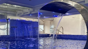 Una piscina interior moderna con paredes de azulejos azules y un elemento acuático central.