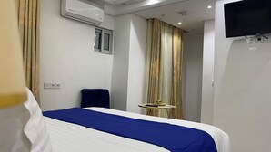 Una habitación de hotel con cama, una silla, una mesita, televisión y aire acondicionado.