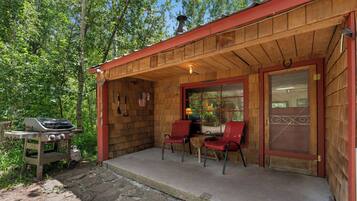 Une cabane en bois avec un porche, deux chaises rouges, un barbecue et un drapeau américain.