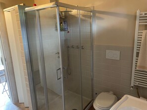 Une douche en verre, avec des toilettes et un porte-serviettes, dans une salle de bain.