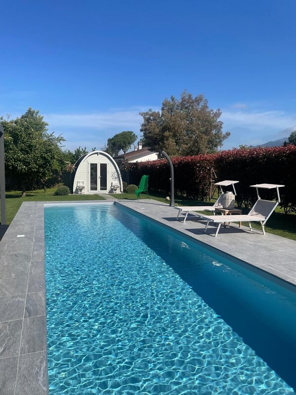 Une piscine rectangulaire à l’eau d’un bleu limpide, entourée d’une terrasse carrelée. On y trouve des chaises longues et une petite table.