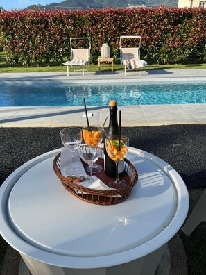 A poolside table with a bottle of champagne, two glasses, and a basket with fruit. - Villa Francesca, pool (Capanne-Prato-Cinquale)