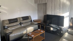 A modern living room with a leather sofa, a wooden coffee table, a flat-screen TV, and a pendant light. - Ratcliffe House (Sileby)