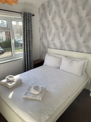 A neatly made bed with white linens, a window with curtains, and a patterned wall. - Ratcliffe House (Sileby)