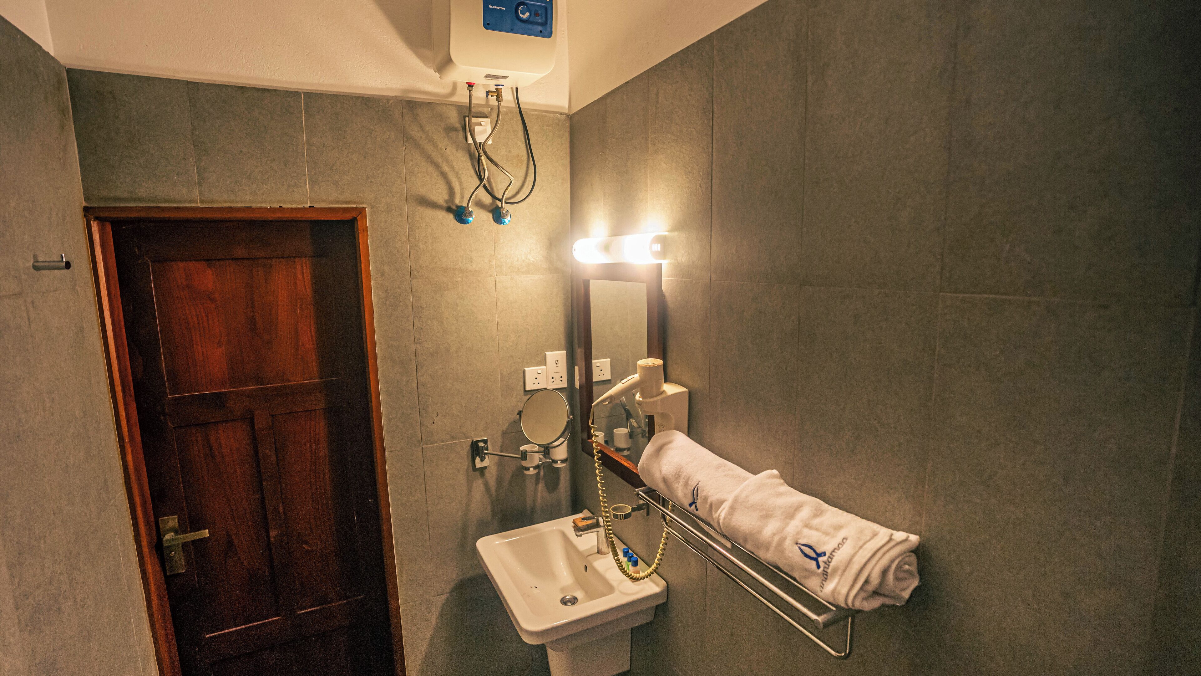 Un bany amb una porta de fusta, un lavabo, un mirall i un escurapulides.