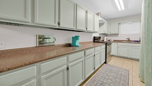 A kitchen with white cabinets, a granite countertop, a coffee maker, and a stove. - Cute, Comfy & Walkable 2/2 Condo Central McAllen (McAllen)