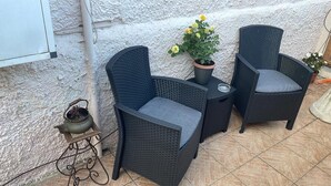 Een terras met rieten meubilair, een klein tafeltje en een bloempot.