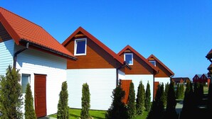 A row of modern houses with red roofs and white exteriors, surrounded by well-maintained lawns and trees.