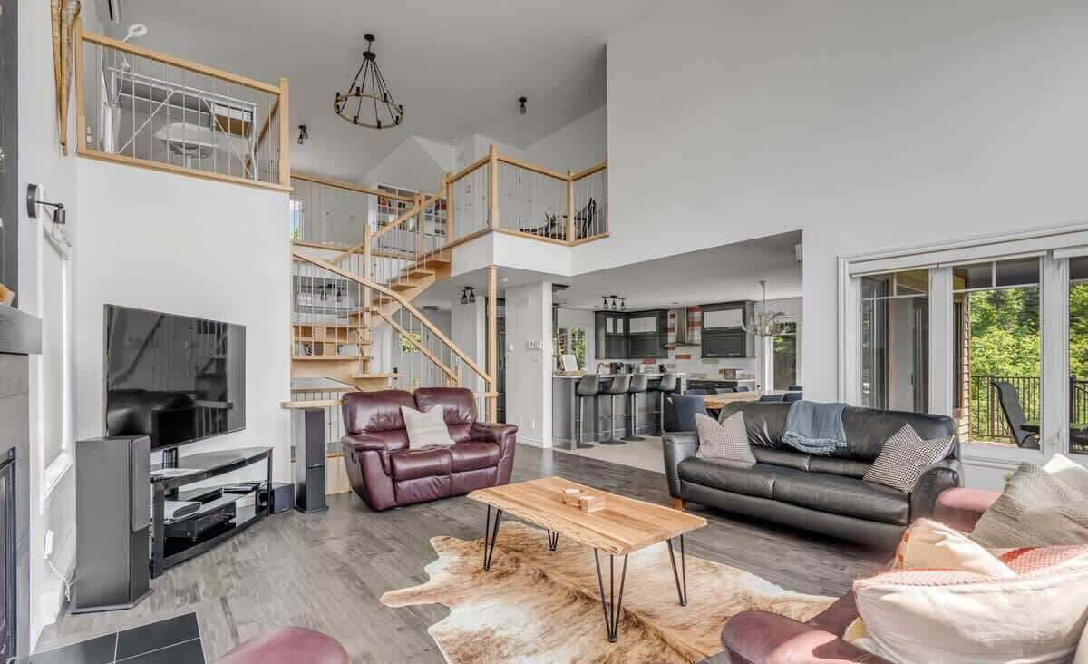 A spacious living area with a staircase, leather sofas, a wooden coffee table, and a television.