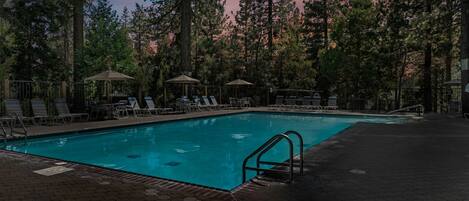 A swimming pool surrounded by lounge chairs and umbrellas, set in a wooded area.