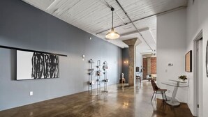A spacious gallery with a large abstract painting, modern art installations, and a dining area with a glass table and chairs. - Urban Opulence Loft | Rogers Place | UG Parking (Edmonton)
