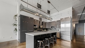 A modern kitchen with a central island, stainless steel appliances, and bar stools. - Urban Opulence Loft | Rogers Place | UG Parking (Edmonton)