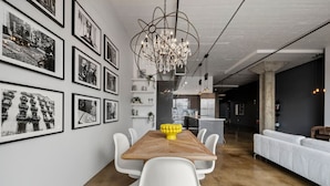 A modern dining area with a wooden table, white chairs, and a chandelier. - Urban Opulence Loft | Rogers Place | UG Parking (Edmonton)