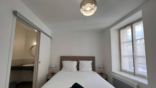 Ein Schlafzimmer mit einem Bett, Nachttischen, einem Fenster und einer Tür zu einem Badezimmer.