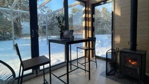 Et moderne interiør med et stort vindue der udover et sneklædt landskab, en pejs og et bord med stole.