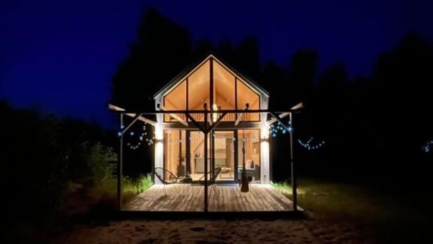 En træhytte med glasfacade, terrasse og lyskæder.