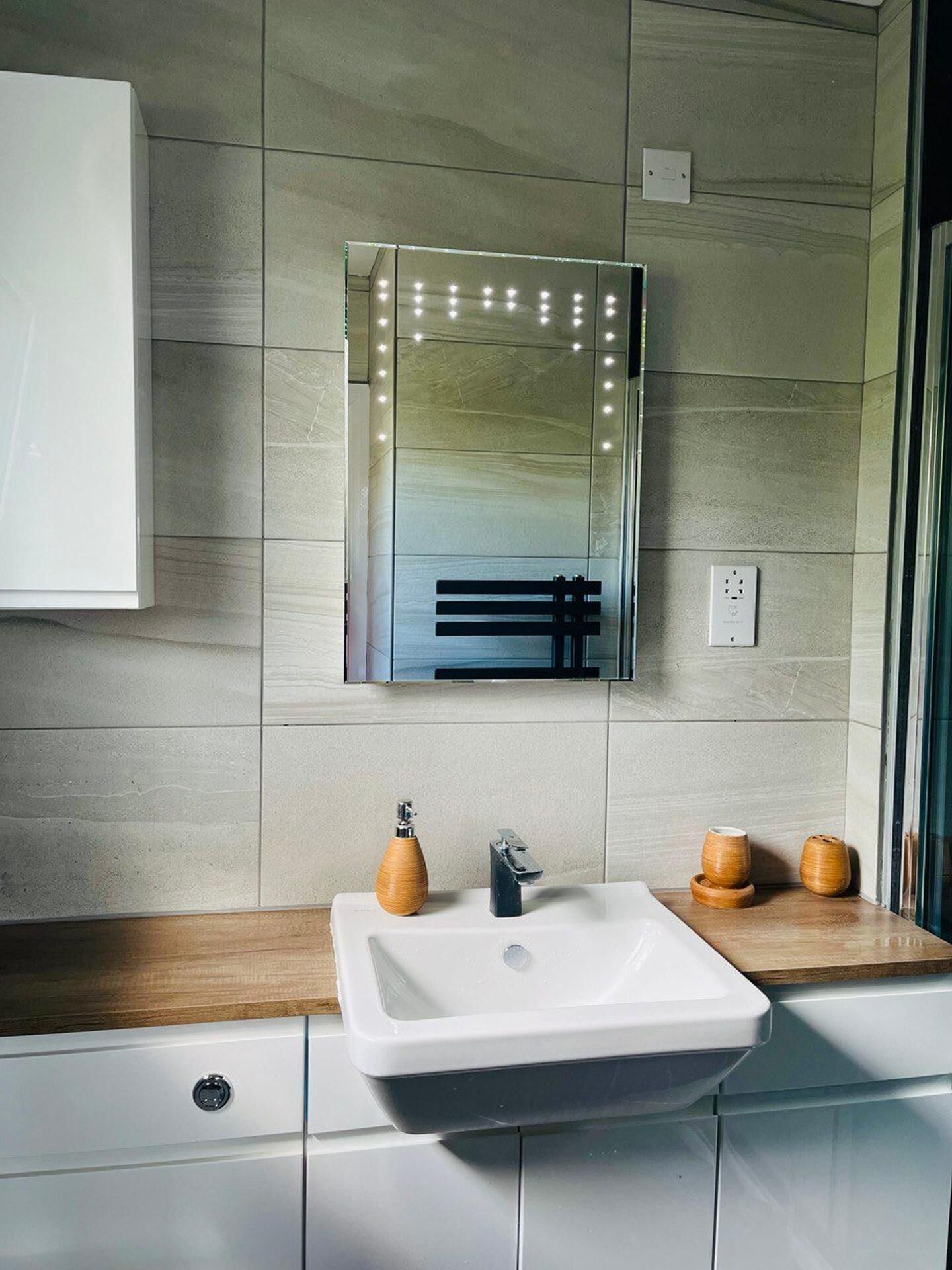 A modern bathroom with a large mirror, a sink, and wooden accents on the countertop.
