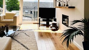 A spacious living room with a large window, a piano, a sofa, and a coffee table. - 4-bed Seaside Dream House - Sleeps 8 & Parking (Dundee)