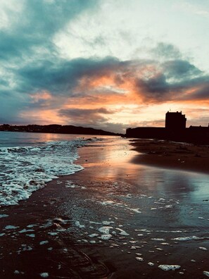 A beach with waves, a distant building, and a cloudy sky. - 4-bed Seaside Dream House - Sleeps 8 & Parking (Dundee)