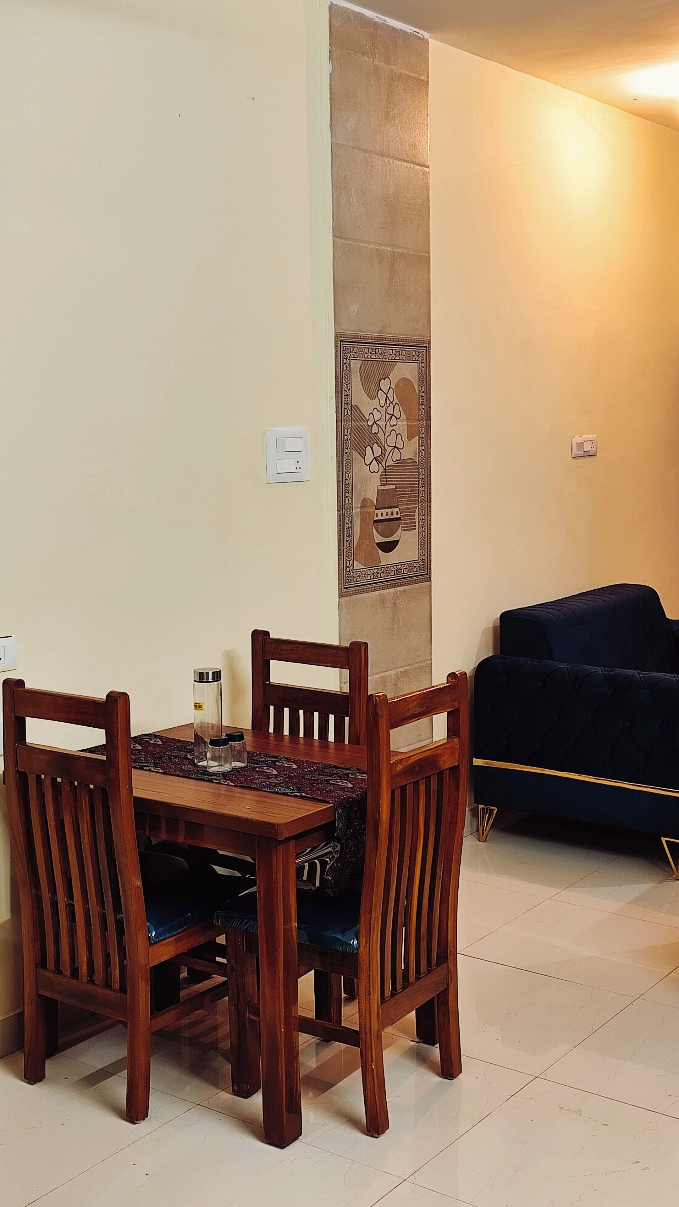 Un comedor con una mesa y sillas de madera, un adorno de pared con estampado y un sofá oscuro al fondo.