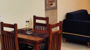 Un comedor con una mesa y sillas de madera, un adorno de pared con estampado y un sofá oscuro al fondo.