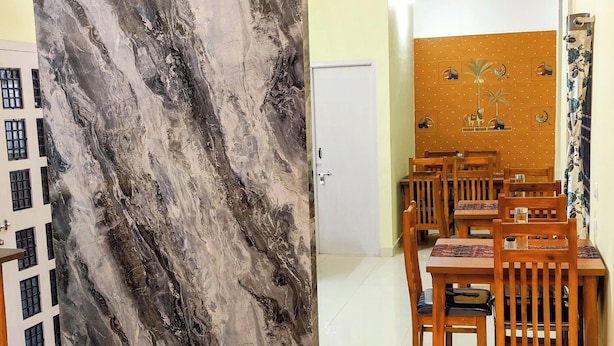 A living room with a blue sofa, a dining area with wooden chairs and a table, and a large marble wall.