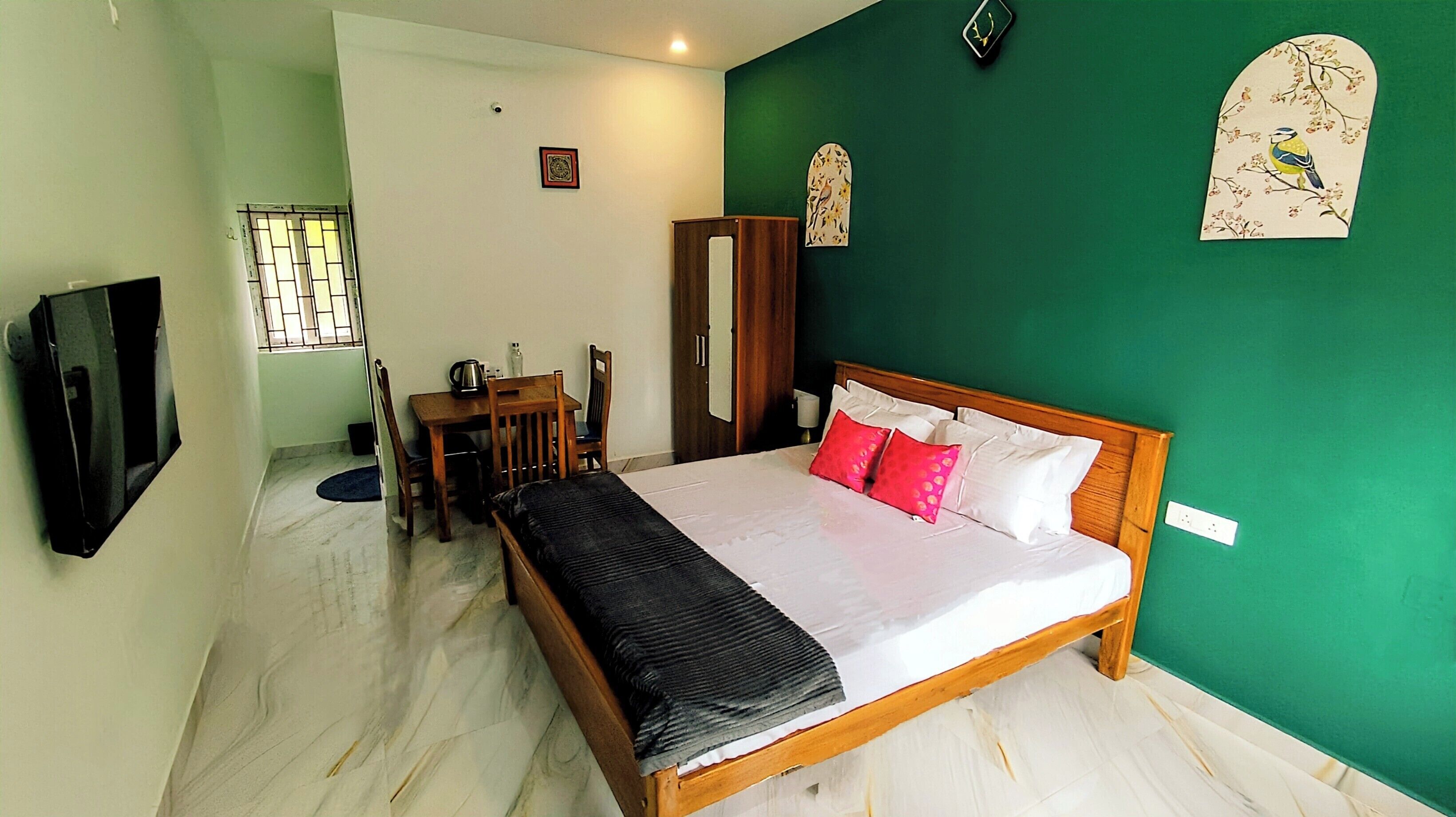 A bedroom with a bed, a desk, and a chair. There is a wardrobe and a television mounted on the wall.