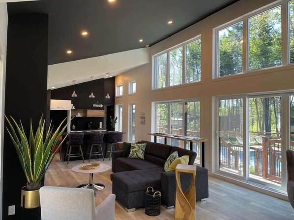 Un espacio habitable amplio con un sofá de color oscuro, una mesa redonda y un ventanal con vistas al exterior.