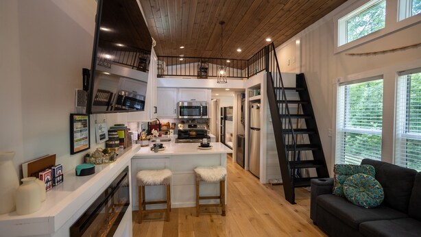 Una cucina moderna con isola centrale, pavimento in legno e zona pranzo in soppalco.