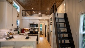 Una cucina con mobili bianchi, un'isola centrale con sgabelli, una scala nera e un soffitto in legno.