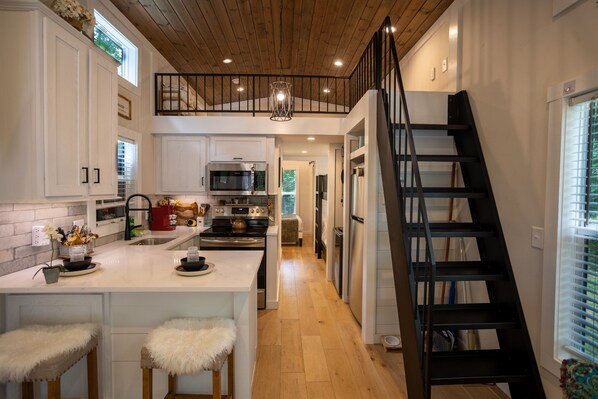 A kitchen with white cabinets, a central island with stools, a black staircase, and a wooden ceiling. - Ryan's World at The Retreat at Sunset Bluff (Monteagle)