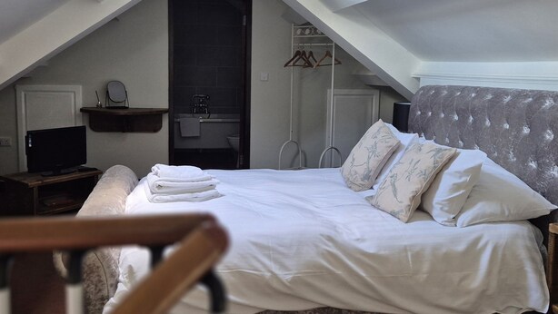 Une chambre à coucher avec un lit, une télévision, une chaise et une salle de bain visible à travers une porte ouverte.