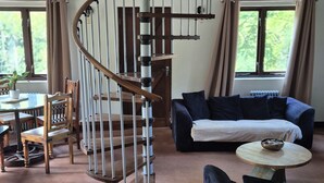 Un salon comprenant un escalier en colimaçon, un canapé, une table basse et un coin repas avec des chaises et une table.